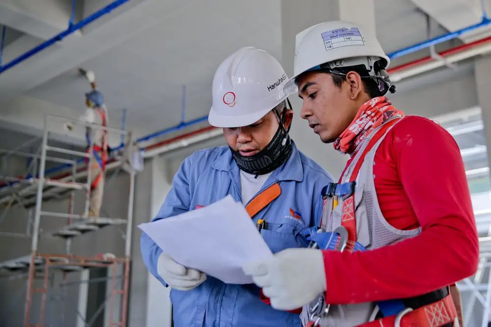 Two workers from different crews reviewing plans on a shared job site